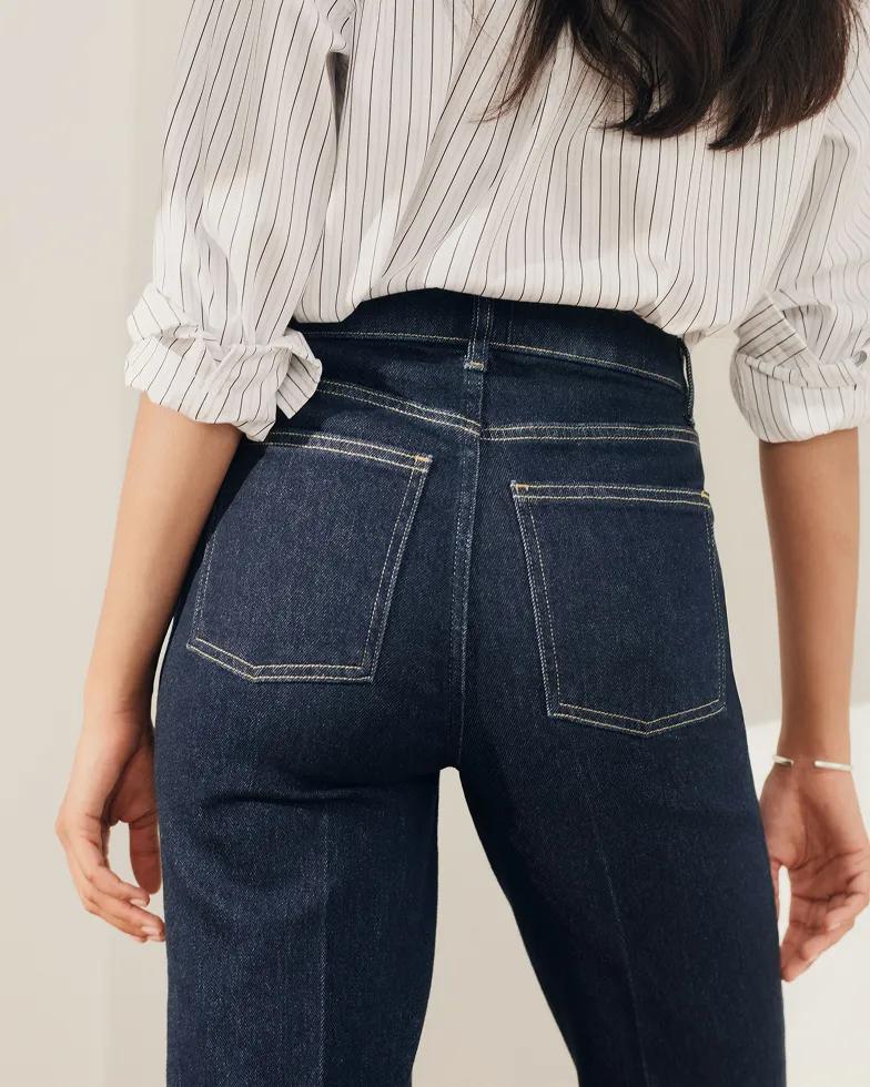 Close-up back view of a model wearing a striped button-down shirt and dark-wash high-rise jeans, highlighting the back pocket detailing.