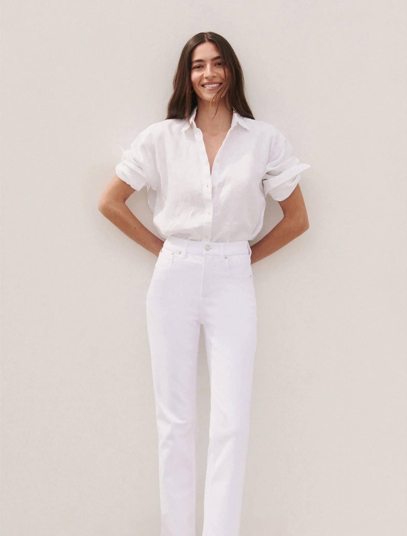 Model wearing white straight-leg jeans with a relaxed white linen button-down shirt, styled in a full-length tonal look