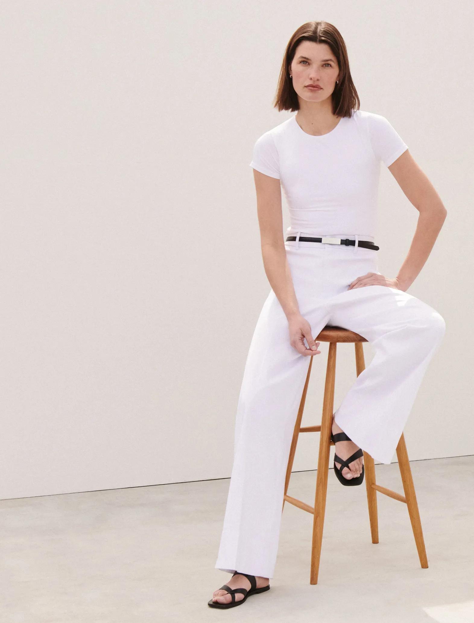 Model wearing white wide-leg pants and a fitted white crewneck tee, styled with a slim black belt and black strappy sandals