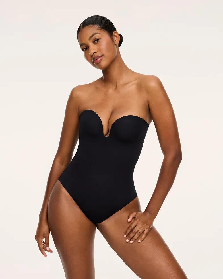Model wears a black strapless plunge bodysuit with a V-shaped underwire cup, seamless smoothing fabric, and a scoop-back silhouette.