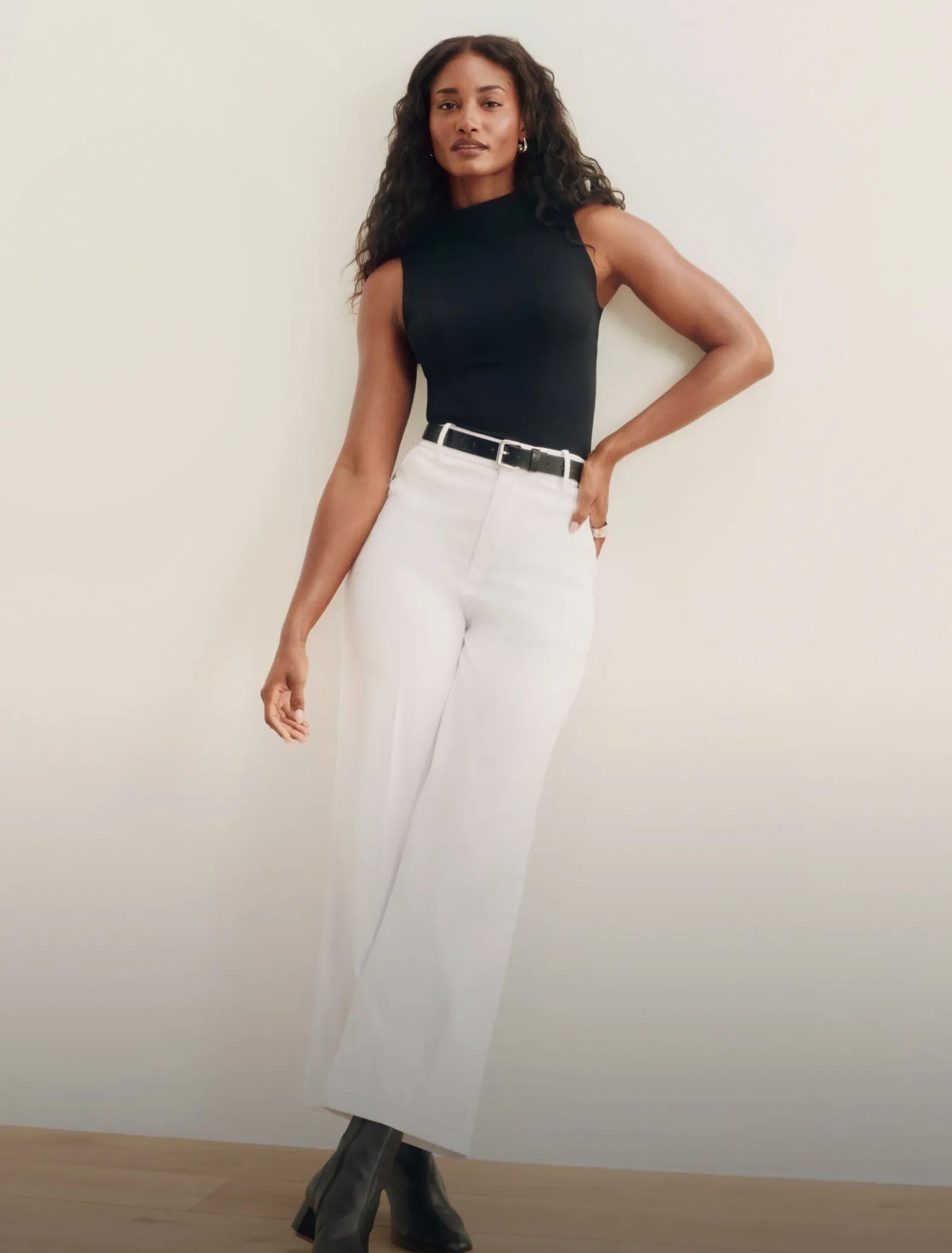 woman in black spanx top and white stretch twill pants standing against the wall