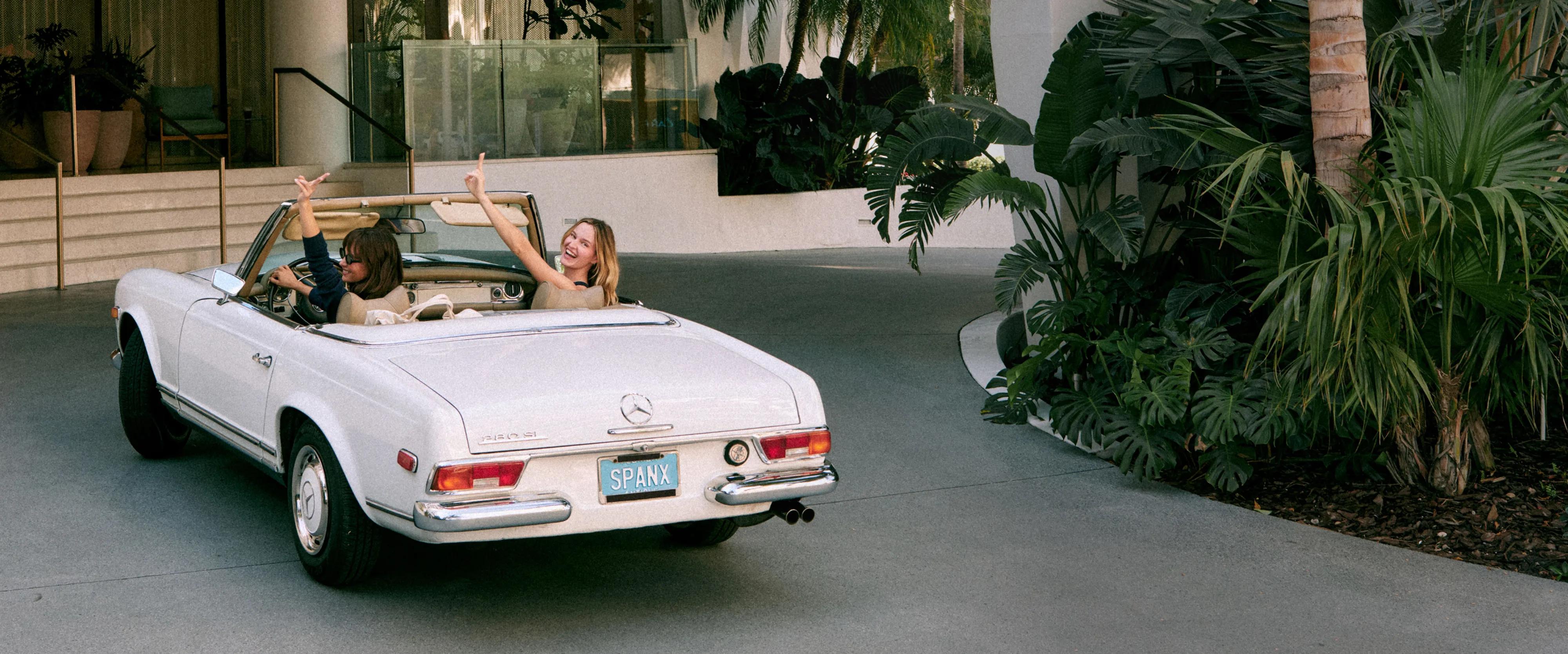 SPANX — two women celebrating in a vintage white convertible, one in a navy top, one in a tan top