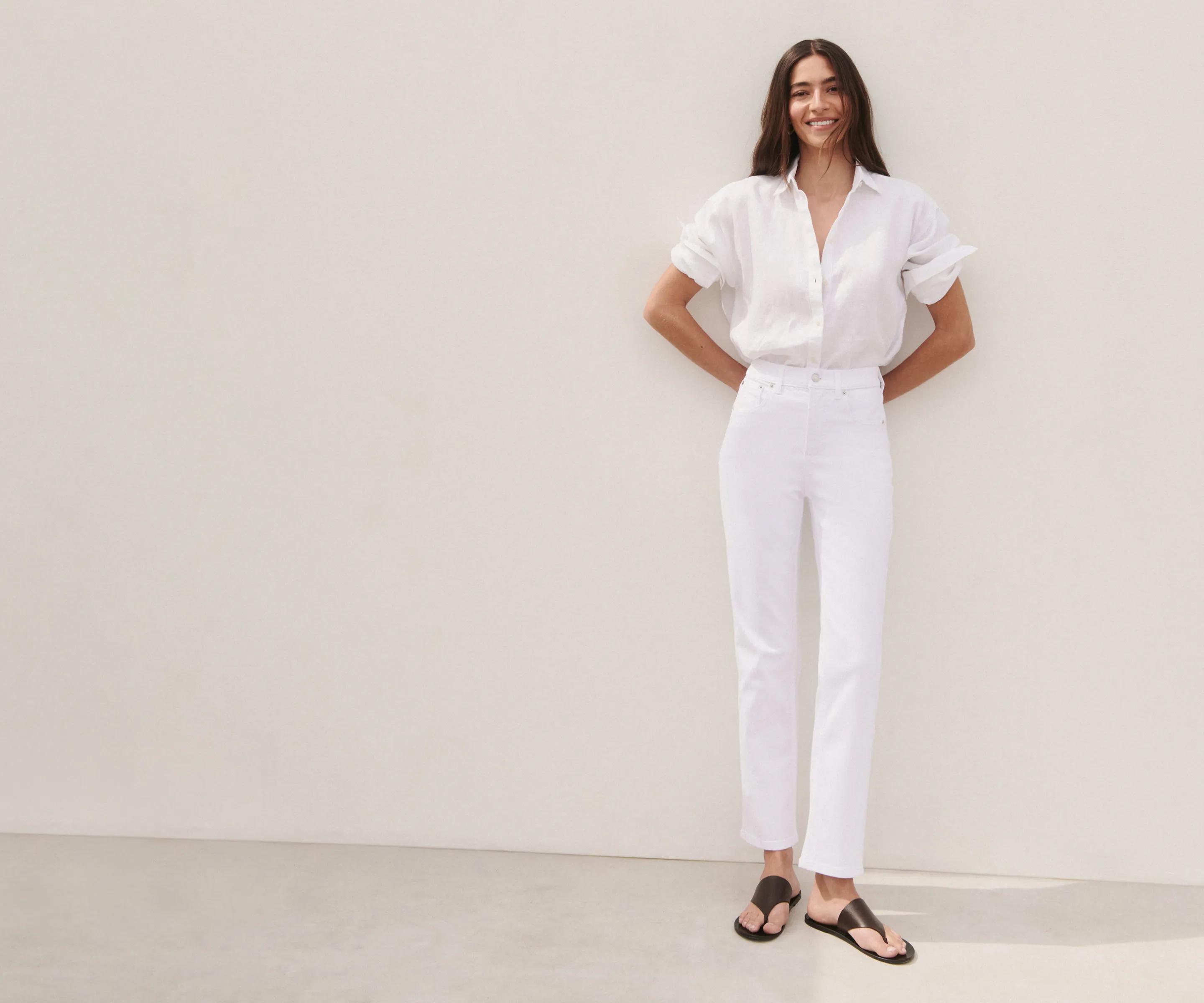 Model wearing white straight-leg jeans with a relaxed white linen button-down shirt, styled in a full-length tonal look