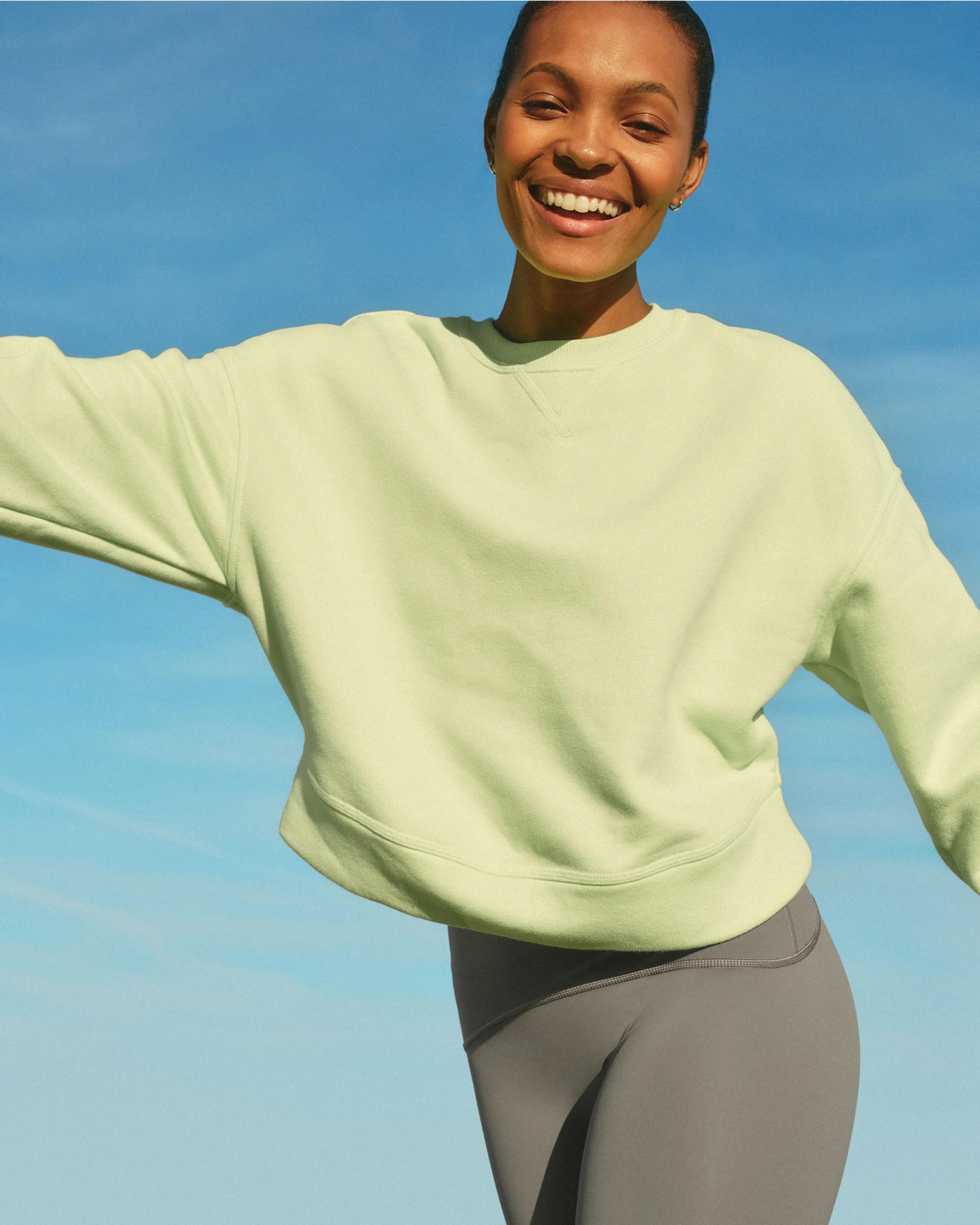 Model wearing a citron green oversized crewneck sweatshirt paired with slate gray leggings against a bright blue sky