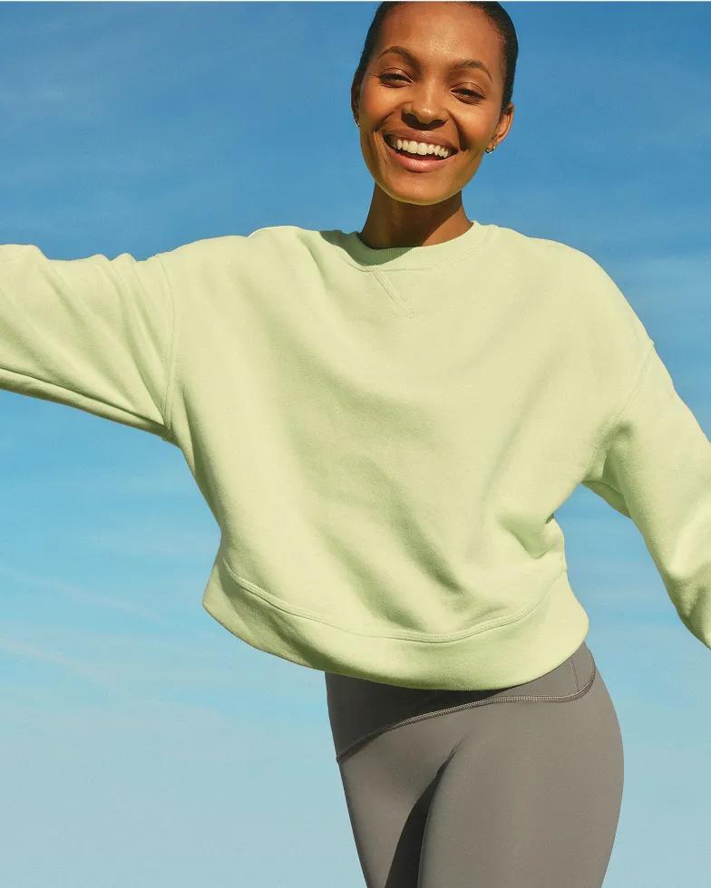 Model wearing a citron green oversized crewneck sweatshirt paired with slate gray leggings against a bright blue sky