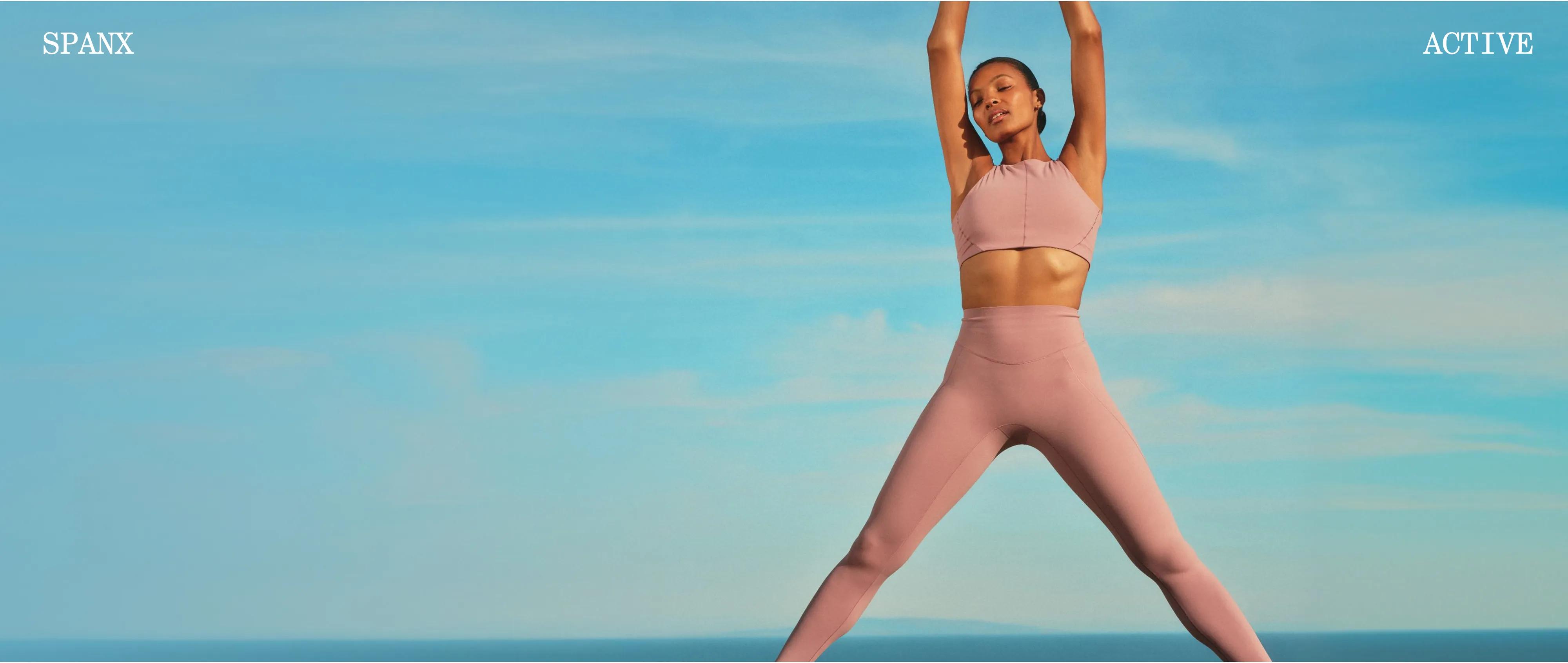 Model wearing a mauve pink halter sports bra and matching high-waist leggings against a bright blue sky