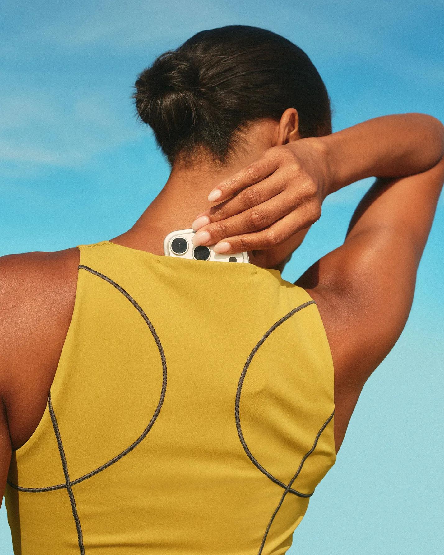 woman in spanx run club tank in pear putting her phone in her back tank pocket