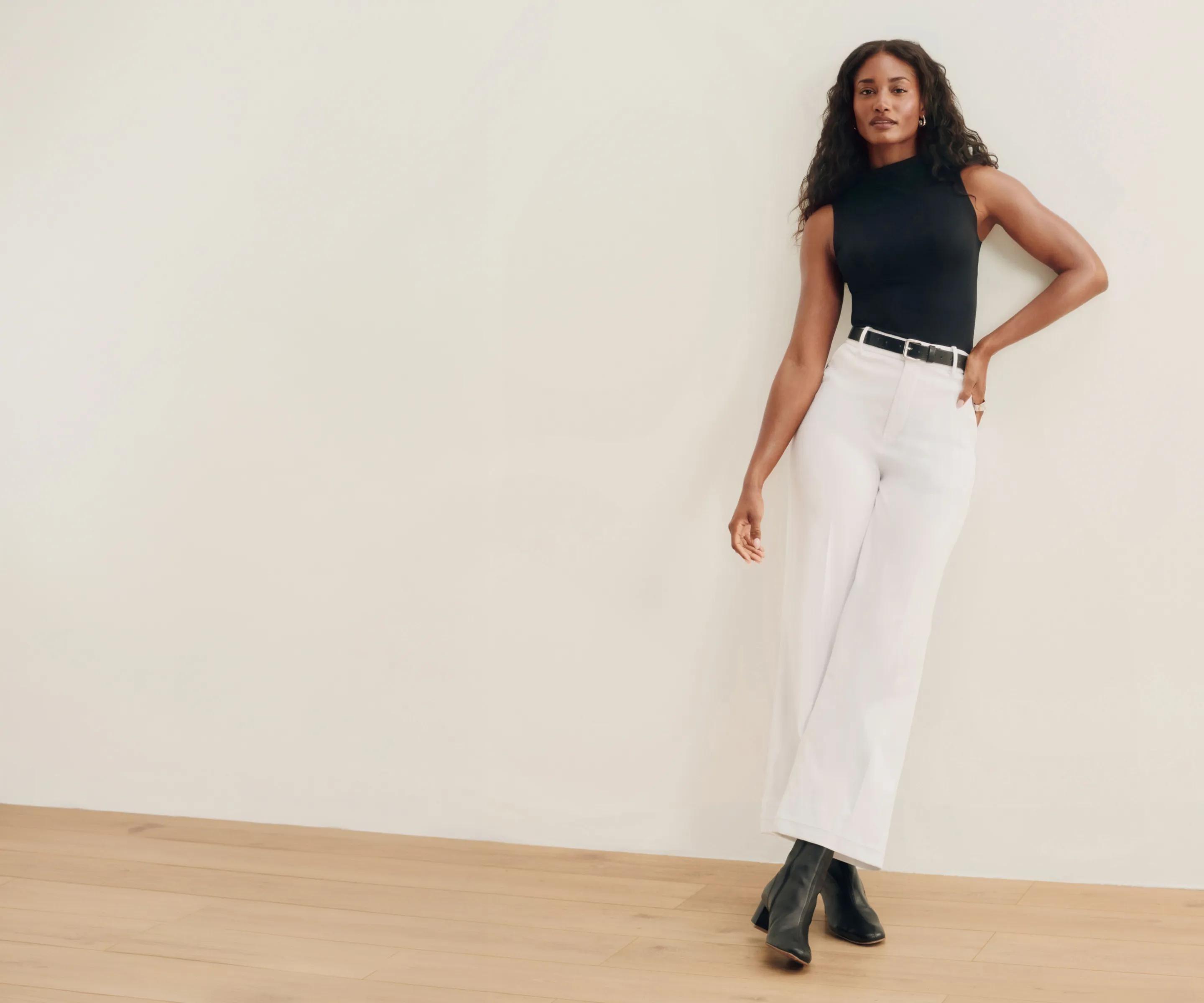 woman in black spanx top and white stretch twill pants standing against the wall