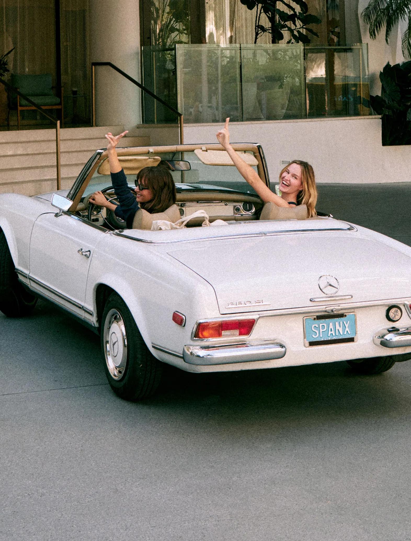 SPANX — two women celebrating in a vintage white convertible, one in a navy top, one in a tan top