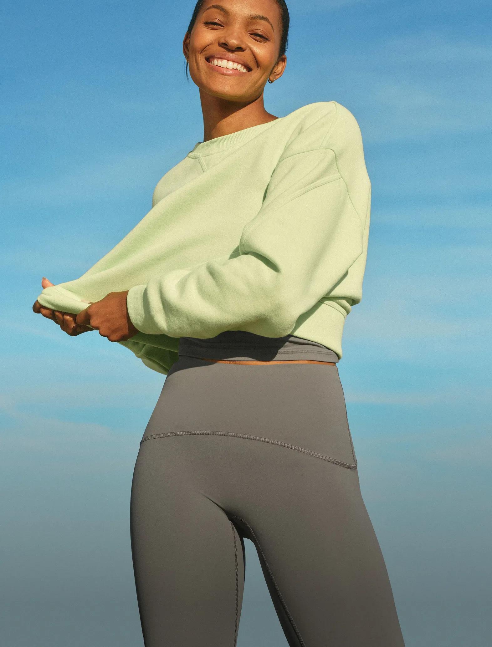 Model wearing a citron green oversized crewneck sweatshirt paired with slate gray leggings against a bright blue sky