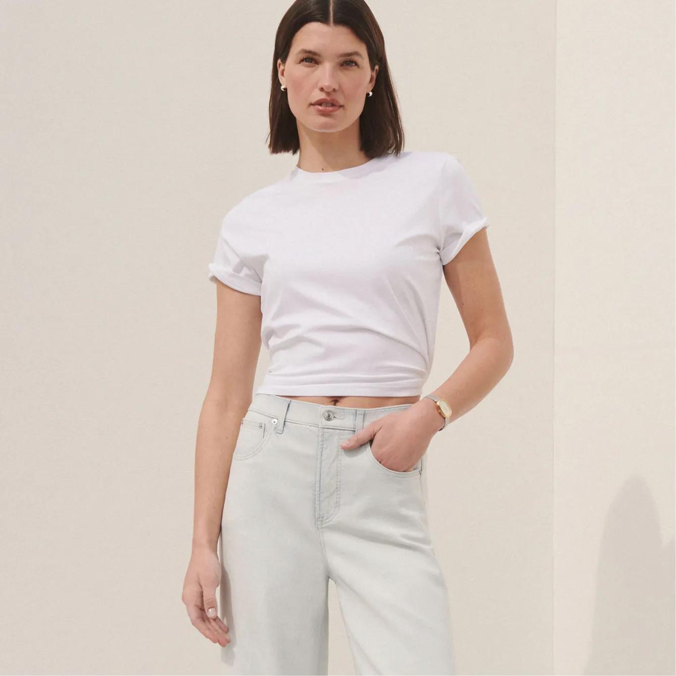 Model wears a white cropped crew-neck t-shirt with rolled sleeves, paired with light-wash high-rise wide-leg jeans.
